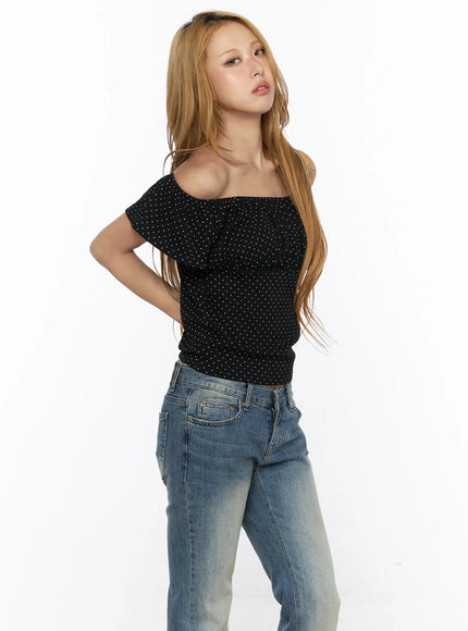 Polka Dot Frill Two-Way Tee CL528 Black side shot on model wearing one-shoulder style, hand in hair, carrying black bag, styled with wide-leg blue jeans and studded belt