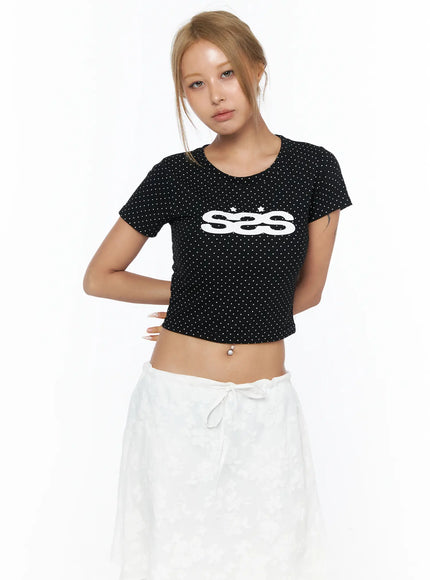 Polka Dot Graphic Crop Tee CU523 Black front view on model with bun hairstyle, white polka dot SES logo graphic crop tee styled with white wrap skirt