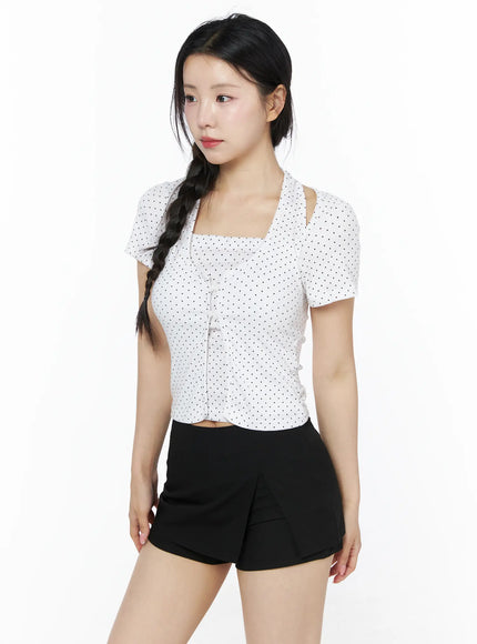 Polka Dot Halter Layered Tee IU525 White three-quarter front shot on model gazing sideways, halter cut-out neckline, polka dot crop top styled with black skort and mini bag