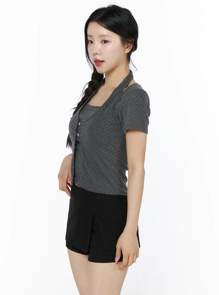 Polka Dot Halter Layered Tee IU525 Grey side shot on model, cut-out halter strap visible at shoulder, dark grey polka dot short-sleeve crop top styled with black mini skort