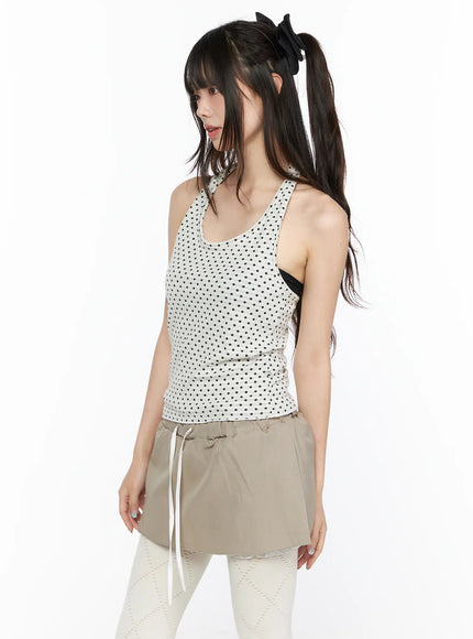 Polka Dot Halter Tank CL523 White three-quarter side shot on model showing scoop neckline and black polka dot knit texture styled with beige drawstring skirt and white tights