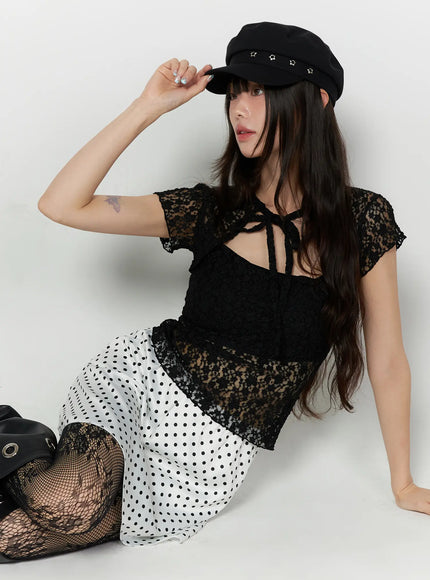 Polka Dot Ribbon Satin Mini Skirt CL522 White editorial seated shot on model wearing baker boy cap holding brim styled with lace top fishnets showing skirt spread on floor