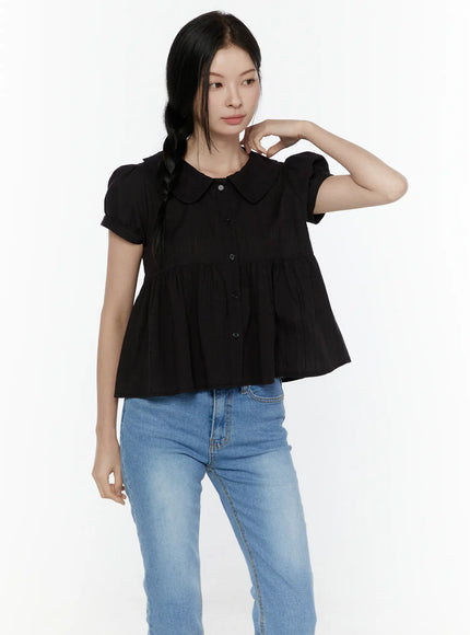 Puff Sleeve Blouse IL506 Black front three-quarter shot on model with hand raised to chin, peter pan collar and button-front peplum blouse, paired with blue straight jeans
