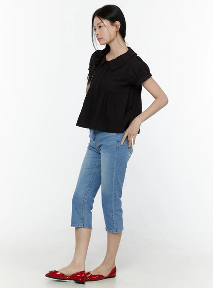Puff Sleeve Blouse IL506 Black side full-body shot on model with hand on hip, showing puff sleeve silhouette, peplum flare, and collar from the side, styled with blue capri jeans
