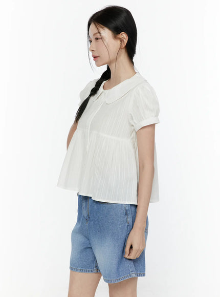 Puff Sleeve Blouse IL506 White side shot on model with braided hair, showing peter pan collar, vertical stripe texture, gathered peplum hem, and puff sleeves, styled with blue denim shorts