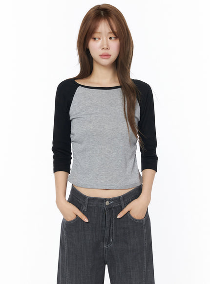 Raglan Shirred 3/4 Top IU525 Gray front close-up on model with long hair, black raglan sleeves, scoop neckline, cropped silhouette, paired with dark wide-leg denim