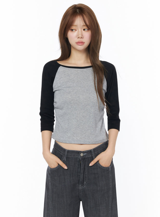 Raglan Shirred 3/4 Top IU525 Gray front close-up on model with long hair, black raglan sleeves, scoop neckline, cropped silhouette, paired with dark wide-leg denim