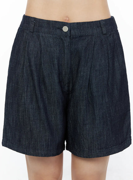 Relaxed-Fit Pintuck Shorts IU525 Dark blue close-up front detail on model showing pintuck pleats silver snap button and denim twill texture