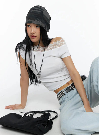 LEWKIN Rhinestone Cross Lace Trim Off-Shoulder Top IL516 White S/M lifestyle front shot model seated on floor wearing camo beanie and cross necklace styled with light blue wide-leg jeans