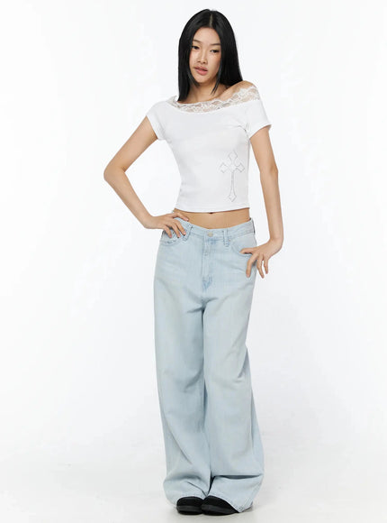 Rhinestone Cross Lace Trim Off-Shoulder Top IL516 White full-length front shot model standing hands on hips showing lace off-shoulder neckline and rhinestone cross detail styled with wide-leg light blue jeans