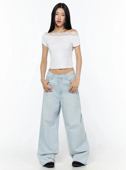 Rhinestone Cross Lace Trim Off-Shoulder Top IL516 White full-length front shot model standing arms relaxed displaying asymmetric lace collar and rhinestone cross motif with wide-leg light blue jeans
