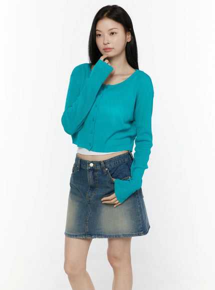Ribbed Crop Cardigan IL506 Teal front three-quarter model shot hand raised to chin ribbed knit crop cardigan with button-front scoop neck long sleeves styled with denim mini skirt