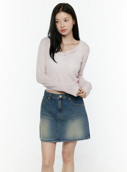 Ribbed Crop Cardigan IL506 Light pink front three-quarter model shot hands clasped ribbed knit scoop neckline crop cardigan with button placket styled with faded denim mini skirt
