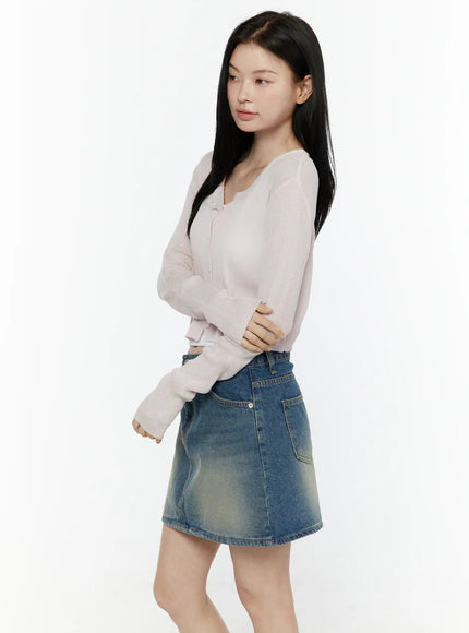 Ribbed Crop Cardigan IL506 Light pink side model shot arms crossed showing ribbed knit texture scoop neckline and long sleeves styled with vintage wash denim mini skirt