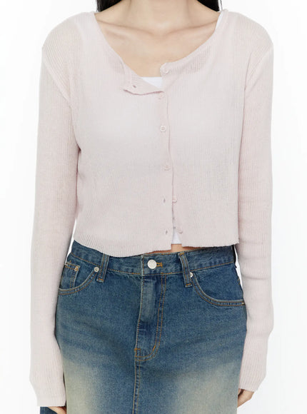 Ribbed Crop Cardigan IL506 Light pink close-up detail shot on model showing scoop neckline button placket ribbed knit fabric and cropped hem with white inner camisole visible
