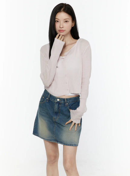 Ribbed Crop Cardigan IL506 Light pink front model shot hand raised to chin headband ribbed knit button-down crop cardigan styled with faded denim mini skirt and white inner tank