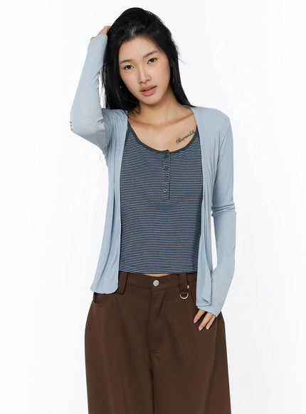 Ribbed Open Knit Cardigan IL509 light blue cropped front shot on model with hand in hair, layered over navy striped cami and brown wide-leg pants, sheer knit texture