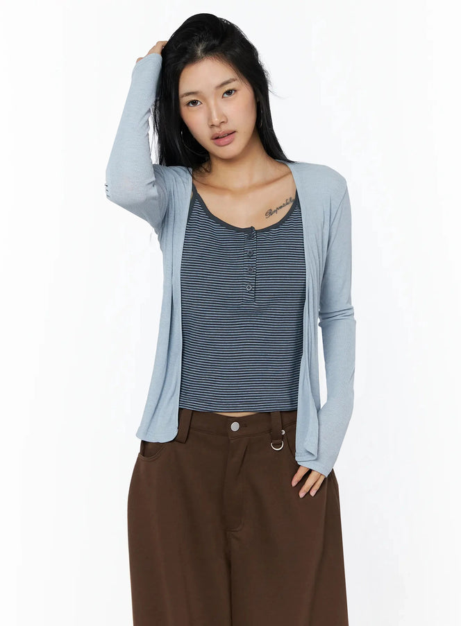 Ribbed Open Knit Cardigan IL509 light blue cropped front shot on model with hand in hair, layered over navy striped cami and brown wide-leg pants, sheer knit texture