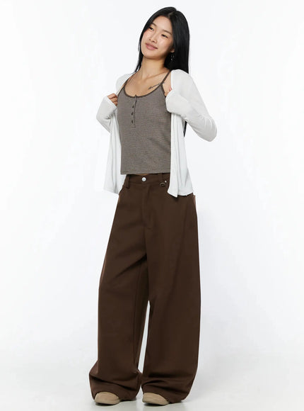 Ribbed Open Knit Cardigan IL509 White three-quarter front shot on model smiling, holding cardigan lapel open, styled with striped cami and brown wide-leg pants