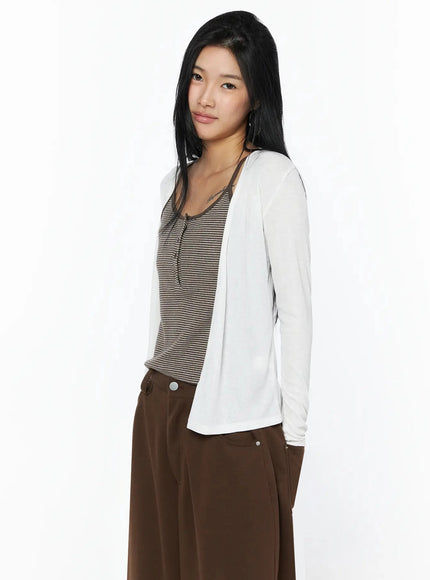 Ribbed Open Knit Cardigan IL509 White side shot on model turned slightly, open-front drape and sheer ribbed knit texture visible, styled with striped cami and brown trousers