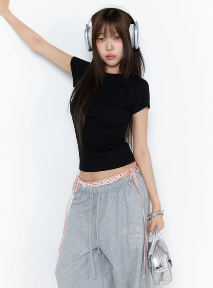 LEWKIN Ribbed Short Sleeve Tee IL515 Black S/M front lifestyle shot model wearing fitted ribbed crop tee with one arm raised styled with gray sweatpants