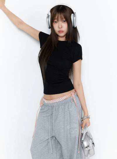 LEWKIN Ribbed Short Sleeve Tee IL515 Black S/M front lifestyle shot model wearing fitted ribbed crop tee with one arm raised styled with gray sweatpants