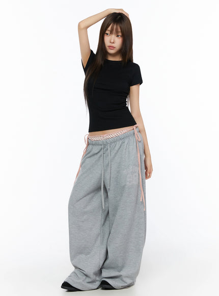 Ribbed Short Sleeve Tee IL515 Black front full-body shot model posing with hand raised above head wearing fitted ribbed crop tee with gray wide-leg sweatpants