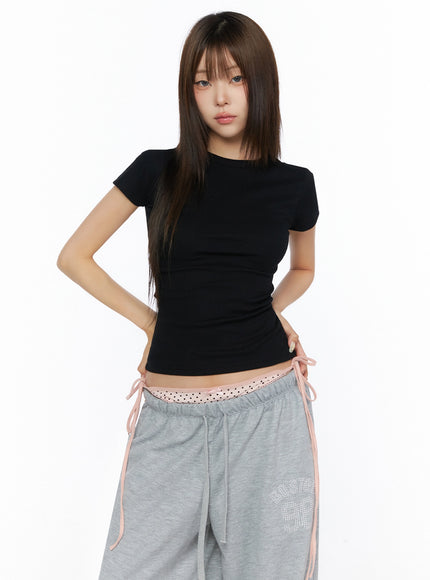 Ribbed Short Sleeve Tee IL515 Black half-body front shot model hands on hips wearing slim ribbed crop tee showing cropped hemline above pink polka-dot waistband