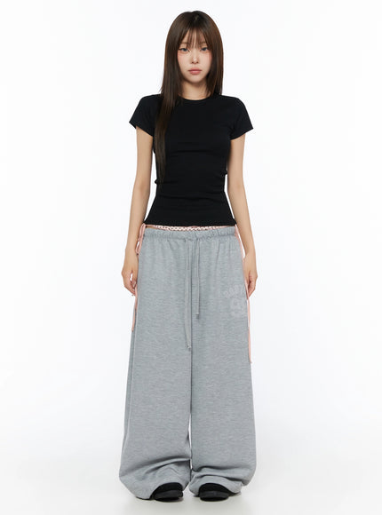 Ribbed Short Sleeve Tee IL515 Black front full-body shot model standing straight facing camera wearing fitted ribbed crop tee styled with gray wide-leg sweatpants