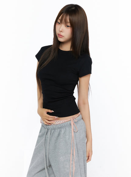 Ribbed Short Sleeve Tee IL515 Black side three-quarter shot model hands clasped at waist wearing slim ribbed crop tee with three-quarter angle view of silhouette