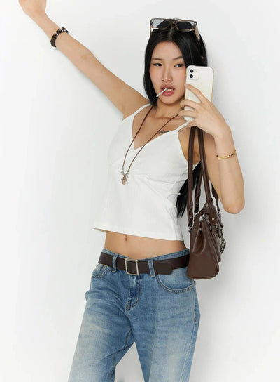 LEWKIN Ribbed Sleeveless Top IL509 White close-up lifestyle shot, model arm raised holding phone, styled with brown belt and low-rise jeans, ribbed wrap-front crop cami