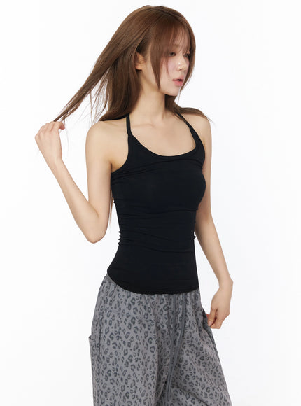 Ribbed Slim Fit Halter Top IU525 Black angled front shot on model touching hair showing halter strap crossover detail and slim silhouette with leopard pants