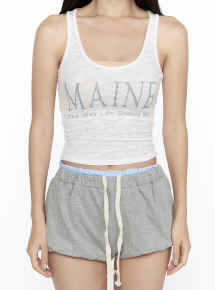 Ribbed Tank Top CL527 White close-up torso shot on model, sheer ribbed knit with full MAINE The Way Life Should Be graphic print visible, paired with gray blue-waistband shorts