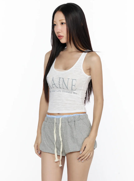 Ribbed Tank Top CL527 White angled front view on model, sheer ribbed MAINE graphic crop tank, three-quarter pose showing scoop neck and midriff, styled with gray drawstring shorts