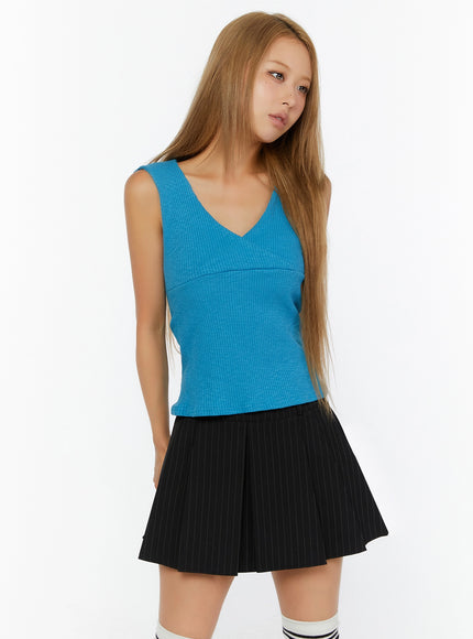 Ribbed Wrap Tank Top IL524 Blue front shot on model, 3/4 angle, V-neck wrap bust detail, ribbed knit texture, fitted silhouette, styled with black pinstripe pleated mini skirt