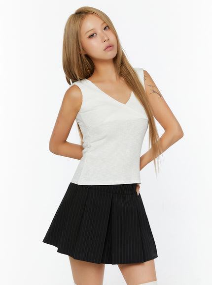 Ribbed Wrap Tank Top IL524 White front shot on model, slight angle, hands behind back, V-neck wrap bust, ribbed knit crop top styled with black pinstripe pleated mini skirt