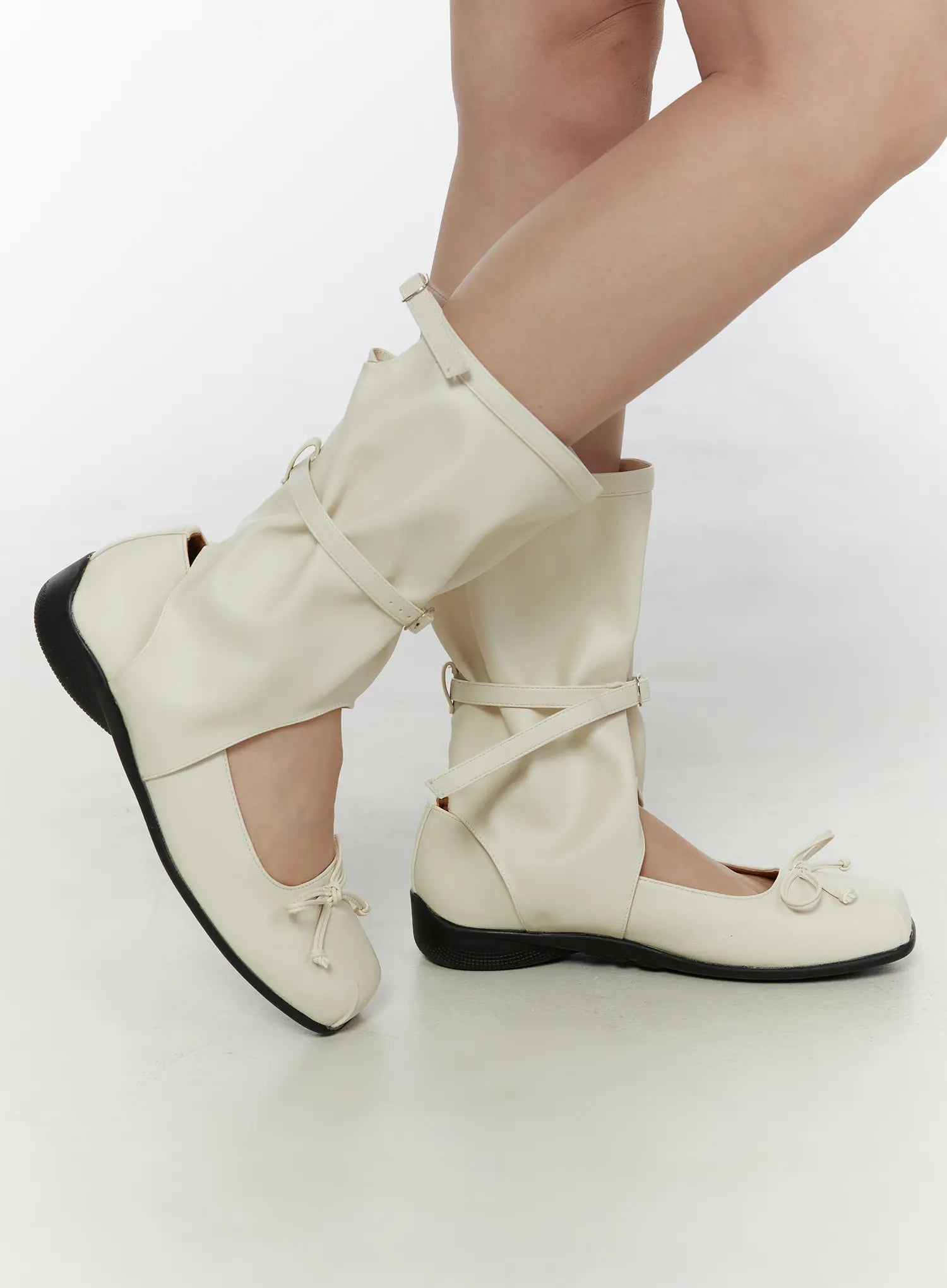 Ribbon Flat Ankle Boots CL507 Light beige dynamic side shot on model with leg raised showing cross buckle strap gaiter cutout and bow toe detail