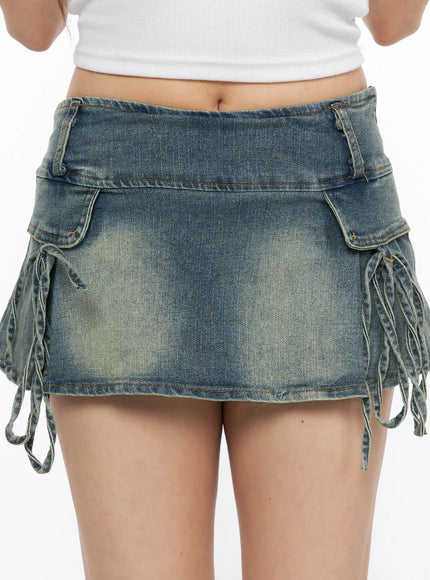 Ribbon Pleated Denim Mini Skirt CL514 Blue close-up front detail on model showing cargo pockets waistband lace-up ribbon ties and vintage yellow-tinted wash denim texture