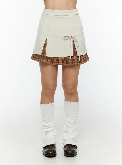 Ribbon Pleated Mini Skirt CU526 Light beige front shot on model showing ribbon tie double split and brown plaid underlayer styled with white leg warmers