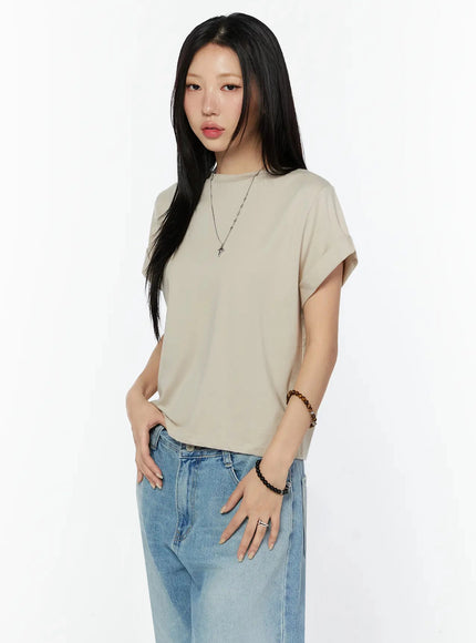 Rolled Cuff Loose Tee IU524 Beige angled side shot on model showing rolled sleeve detail, crew neck, tucked front hem, paired with blue jeans