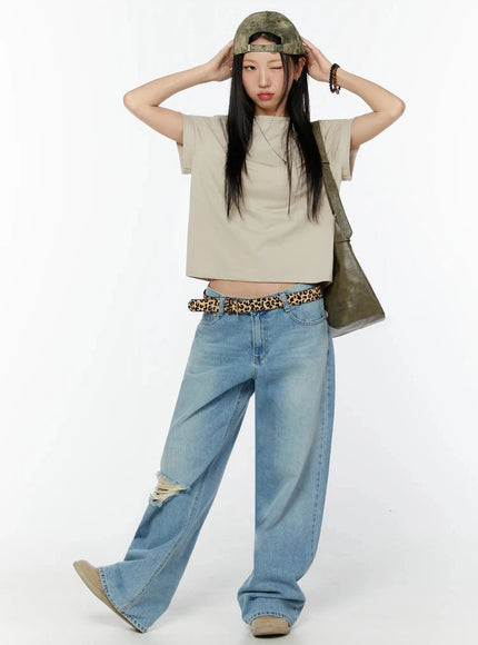 Rolled Cuff Loose Tee IU524 Beige full-body front shot on model adjusting cap, leopard belt, green shoulder bag, ripped wide-leg jeans, walking pose
