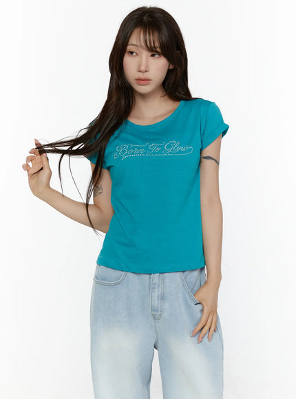 Rolled-Up Graphic Slim Fit Tee CL507 Blue half-body front shot on model tousling hair close-up of rhinestone Born To Glow script lettering on teal cotton fabric