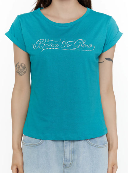 Rolled-Up Graphic Slim Fit Tee CL507 Blue close-up front torso shot on model showing rhinestone Born To Glow script detail and rolled cap sleeves on slim fit teal tee