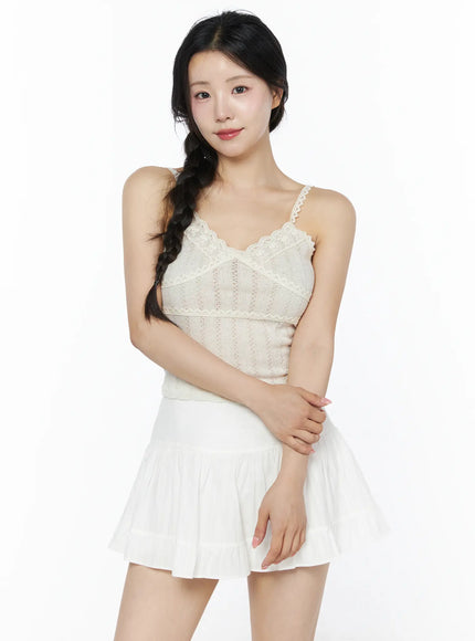 Romantic Lace Cami Top IU525 Light beige front model shot, arms crossed at waist, lace floral V-neckline, semi-sheer pointelle knit fabric, white pleated mini skirt