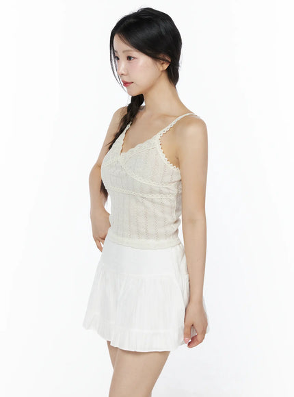 Romantic Lace Cami Top IU525 Light beige side model shot showing slim silhouette, lace shoulder strap, pointelle knit texture, paired with white pleated mini skirt