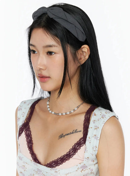 Ruched Bow Headband IL509 Dark gray side-angle close-up on model showing twisted bow structure and fabric texture, worn with lace-trim floral top