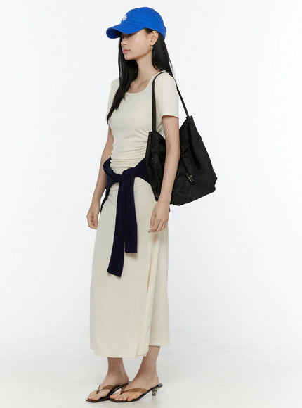 Ruched Maxi Dress IL506 Light beige side model shot styled with navy cardigan tied at waist blue baseball cap black tote bag and thong sandals