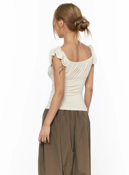Ruched Off-Shoulder Bow Detail Top CU524 light beige close-up back shot on model highlighting ruffle cap sleeves bow shoulder ties and ribbed waist panel