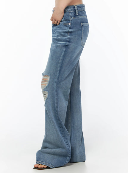 Rue Distressed Bootcut Flare Jeans IU525 Blue side crop shot on model with hand on hip showing single knee distressing and wide-leg flare silhouette