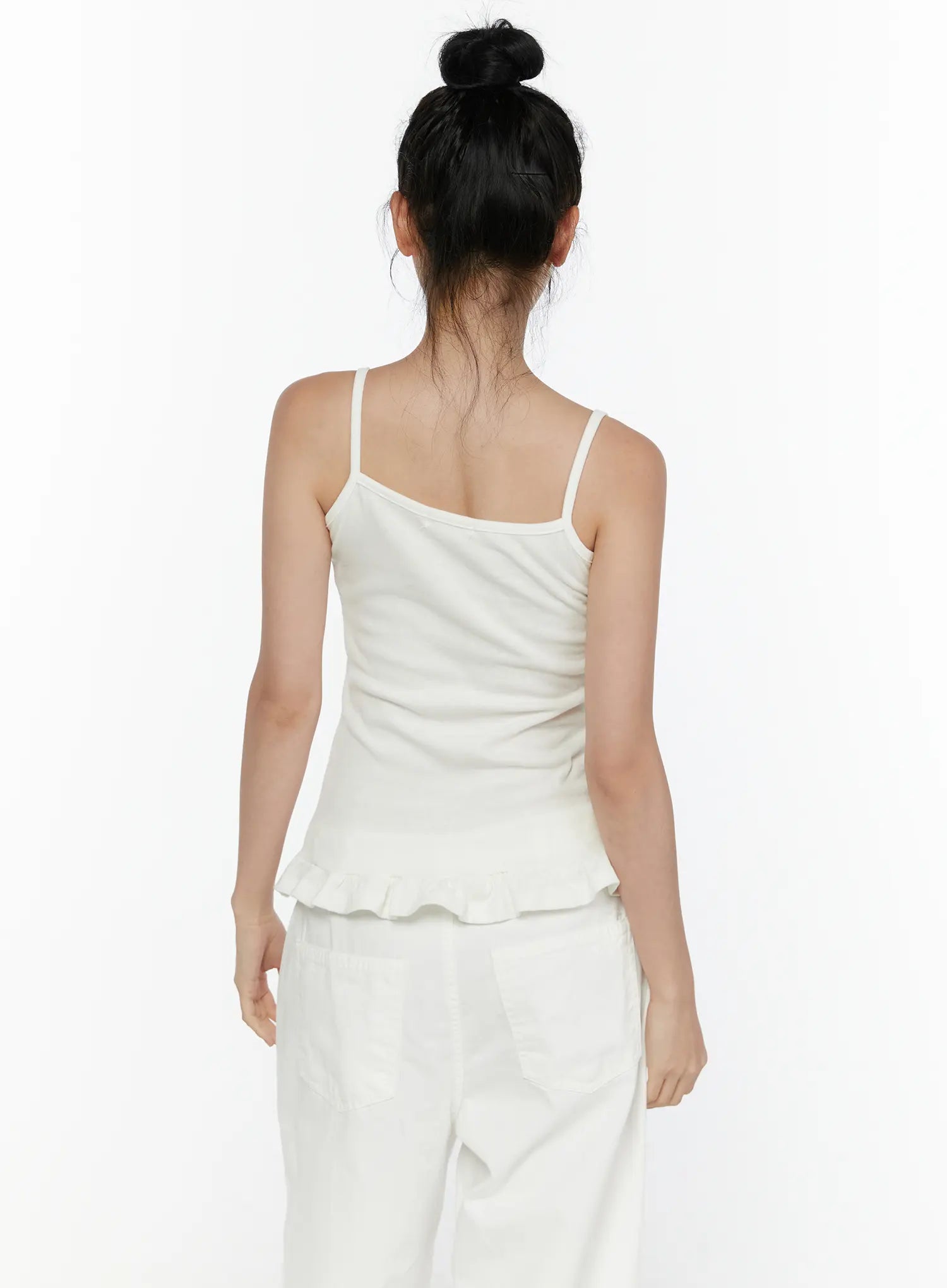Ruffle Detail Cami Top CL521 White back shot on model, spaghetti straps crossing upper back, fitted ribbed knit back, ruffled hem detail at hip level, paired with white trousers
